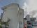 白い２階建ての建物の外壁に灰色の文字で施設の名称が表示されている。建物の周りに樹木が植えられ、車が停められている。