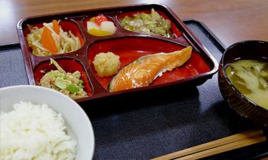 焼き魚やフルーツのデザートが入った重箱とご飯と味噌汁のセット