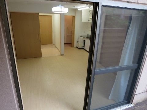 窓の外から撮影された居室の写真。キッチンが備え付けられており、上部には白い扉が付いた収納棚が設置されている。