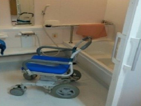 ひじ掛けや青色の座面がついた可動式の椅子が置かれている浴室