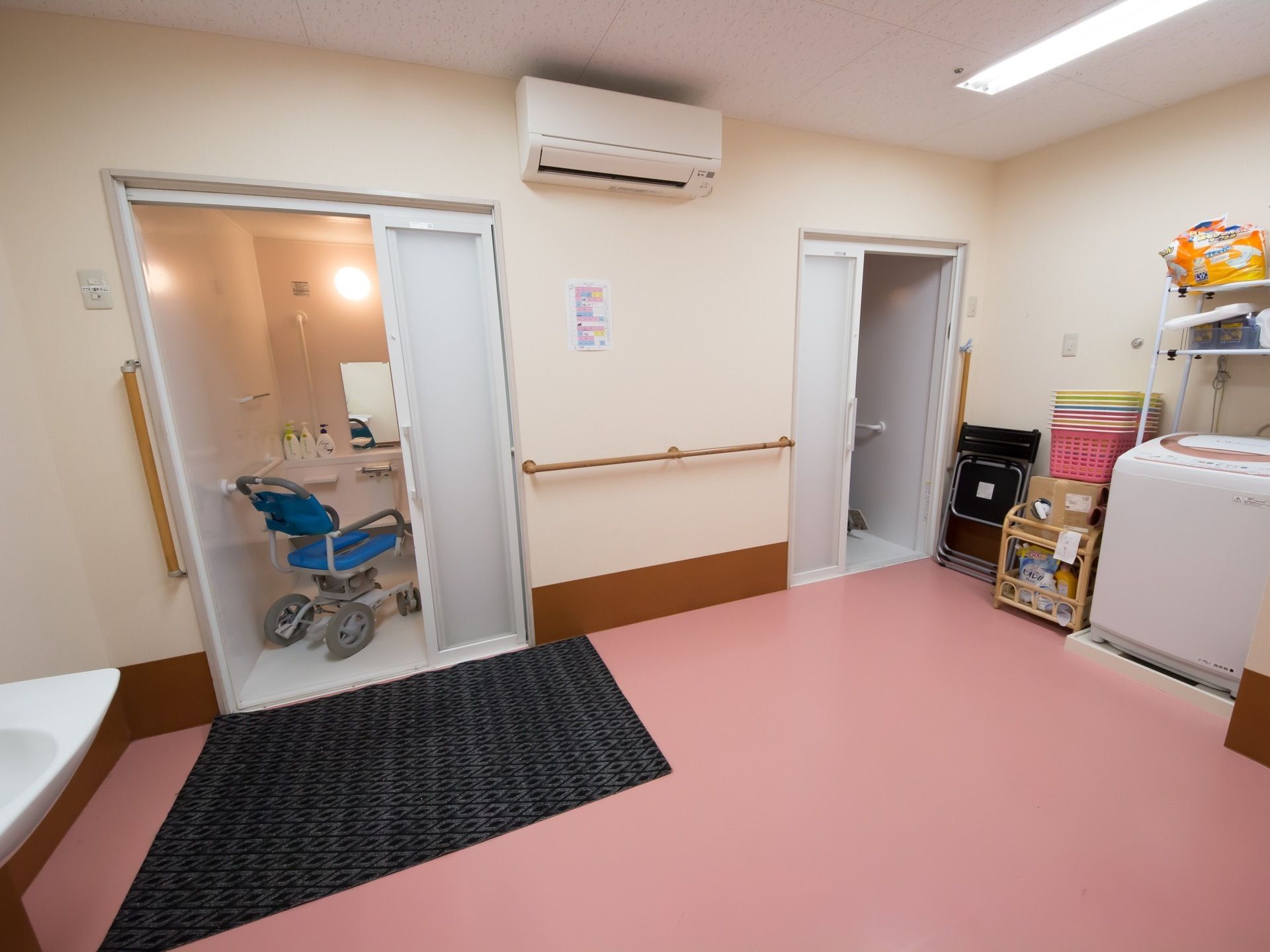 ピンク色の床が印象的なランドリールームである。白色の洗濯機やバスケットなどが備わっている。エアコンも完備している。