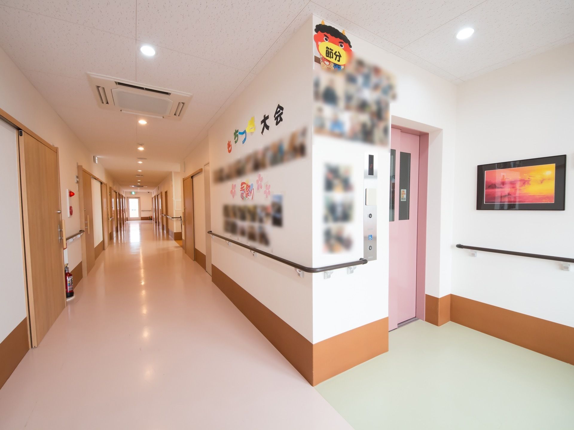淡いピンク色を配した通路で、あたたかい雰囲気がただよっている。壁にダーク系の手すりが備え付けられている。