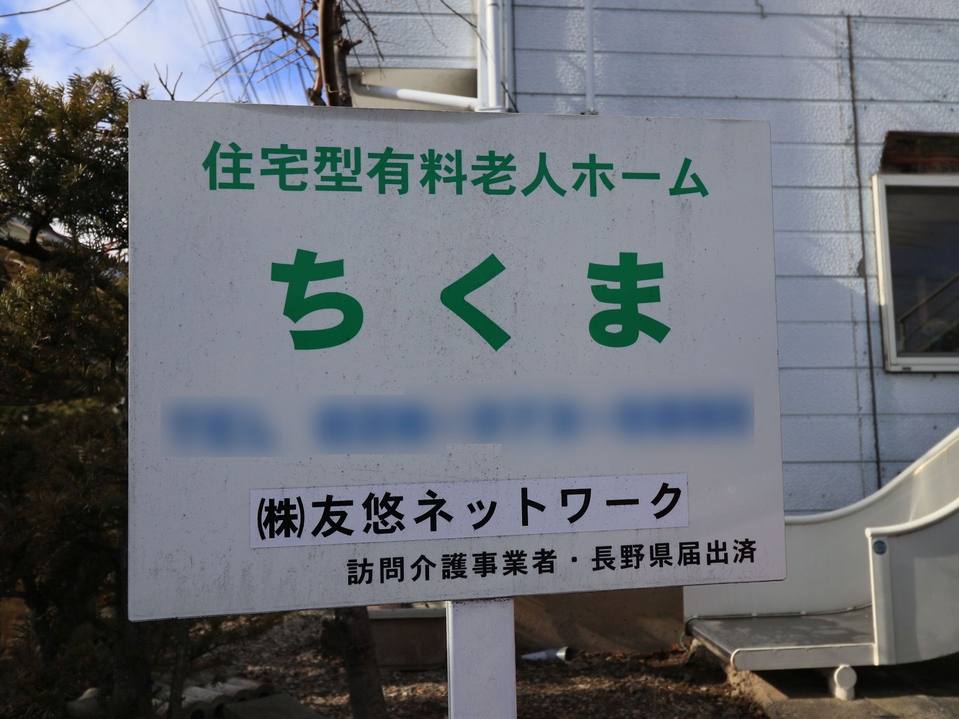 白い看板に緑のゴシック体で施設名が大きく印刷されており、遠くからでも見やすくなっている。施設名の下には会社名が書かれている。