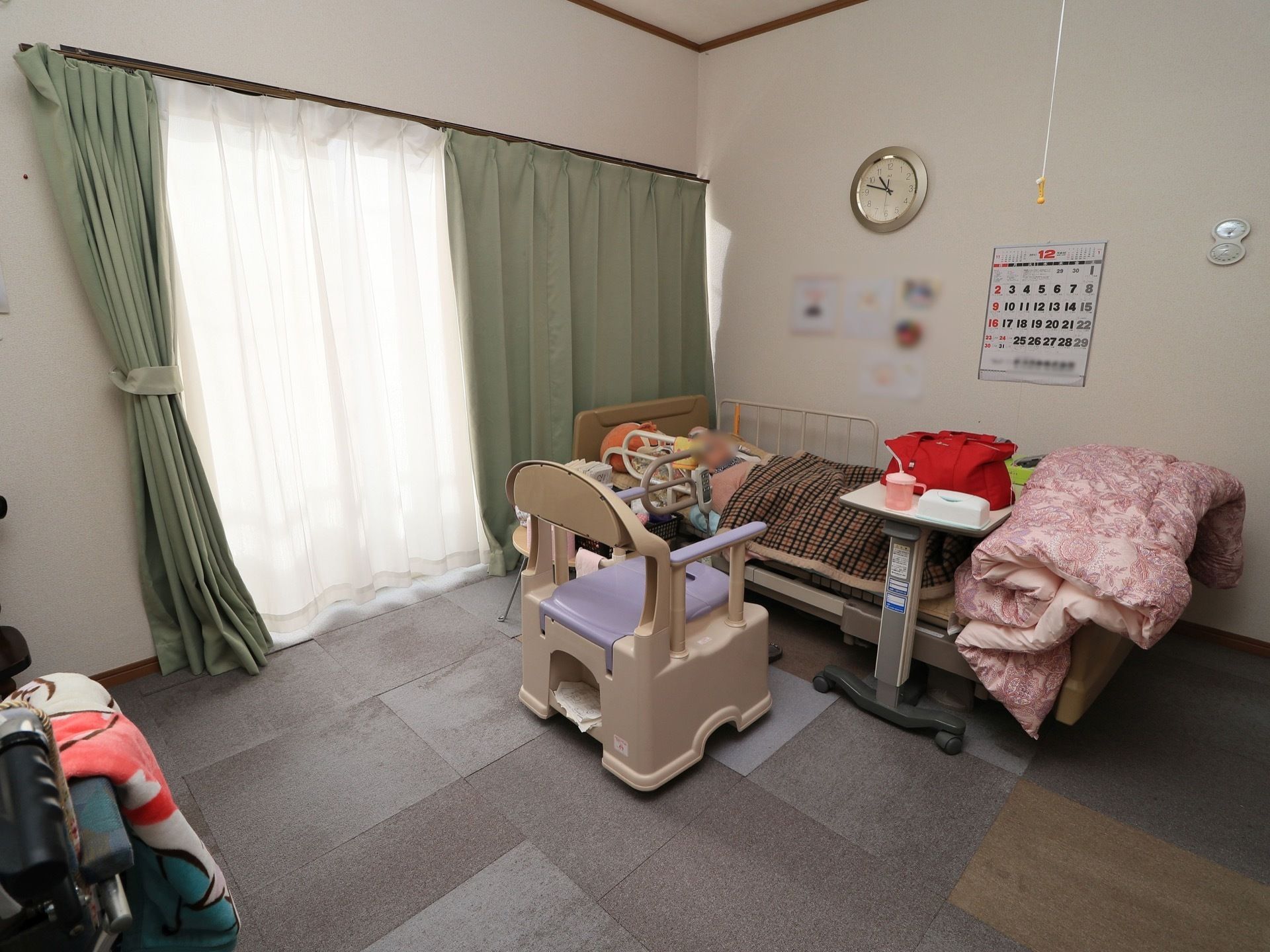 介護用ベッドやポータブルトイレが置かれている居室。窓が大きく取られているため、日の光がたっぷりと入ってくる。
