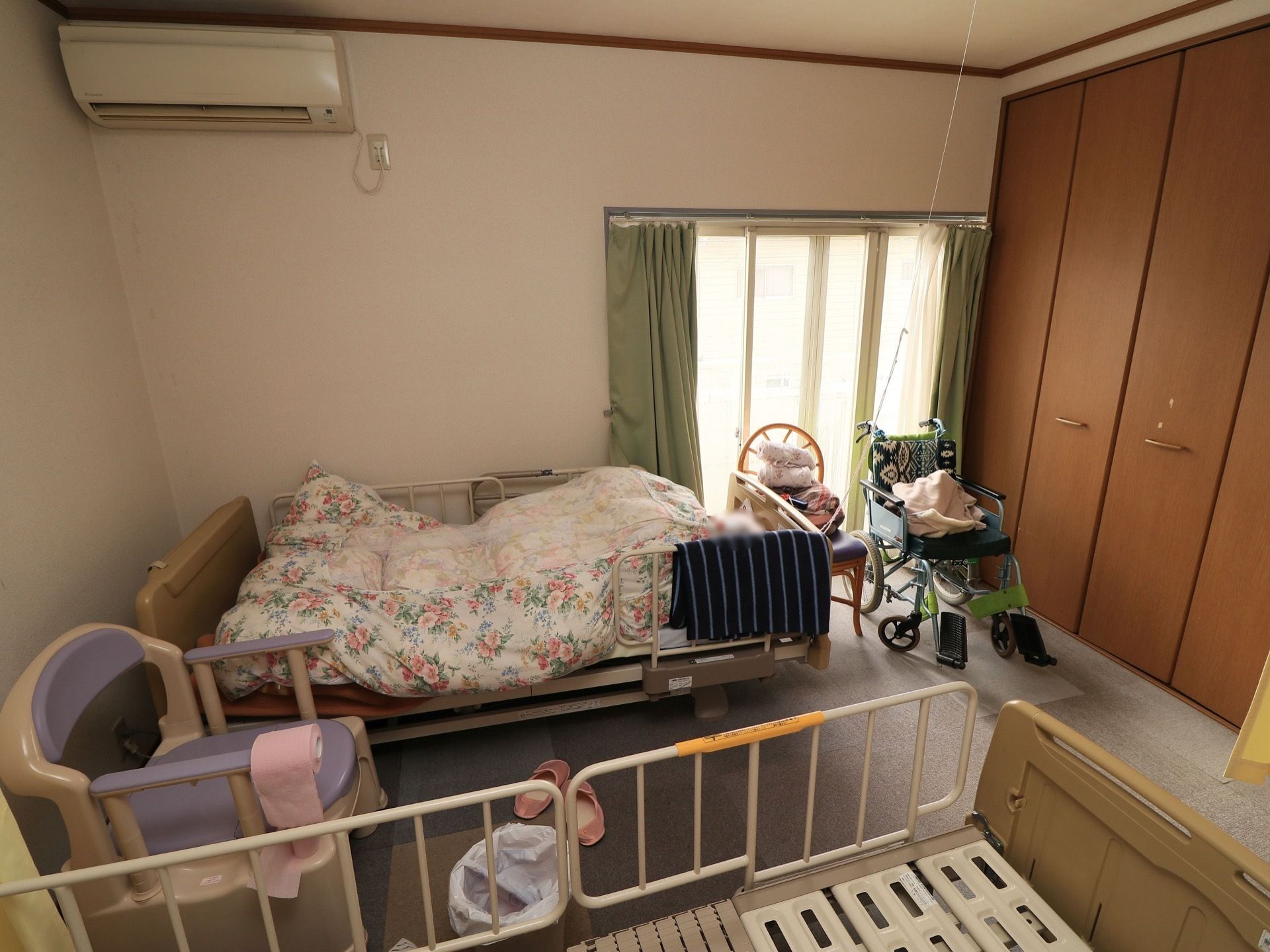 介護用ベッドとポータブルトイレが置かれた居室。クローゼットやエアコンが備えつけられており、快適に過ごせる。