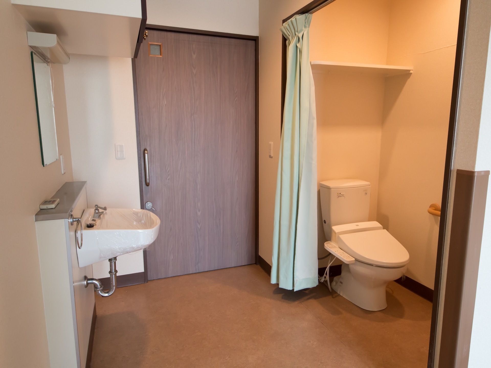 トイレは出入り口と通路が広く、通行しやすくなっている。便器と洗面台の間はカーテンで仕切られ、開け閉めがスムーズに行えるようになっている。