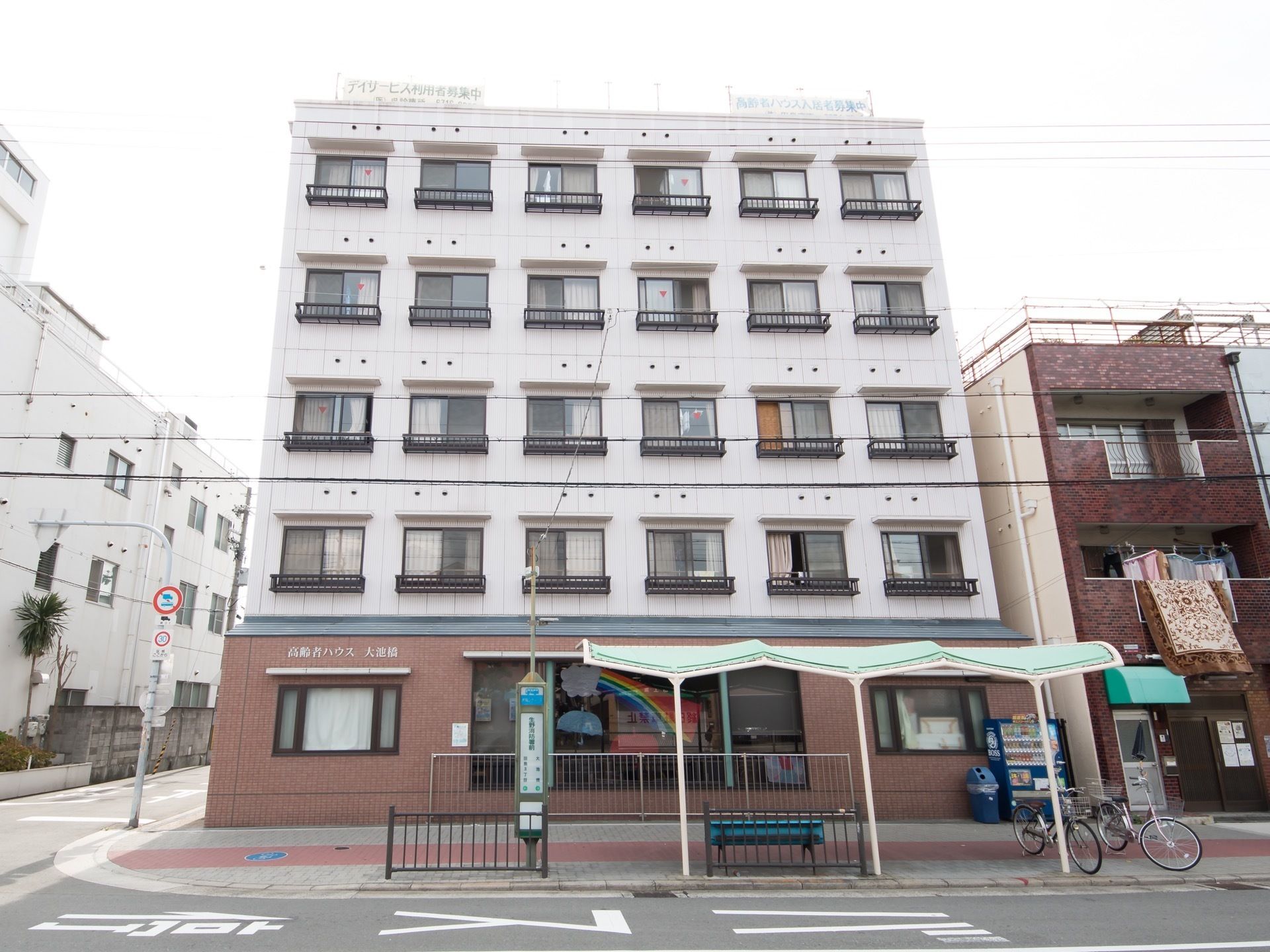 交差点の角に建つ５階建ての建物で、一階部分はレンガ風、二階以上は白色の外壁である。すぐ前にバス停がある。