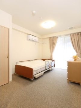 白を基調とした洋室である。電動リクライニング式ベッドとチェストが配置されている。ベッド側の壁にはエアコンが設置されている。