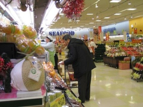 スーパーの生鮮食品売り場である。手前に果物売り場がある。棚には大きなマスクメロンやラッピングされたミカンが並んでいる。