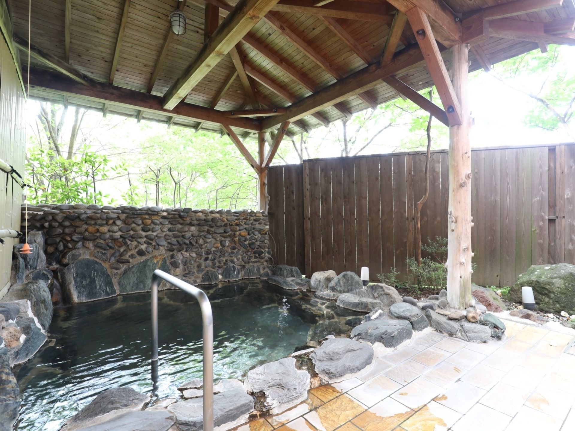 石造りの露天風呂である。木製の屋根とフェンスを設置し、浴槽の出入口に手すりを完備している。周りは緑豊かな風景である。
