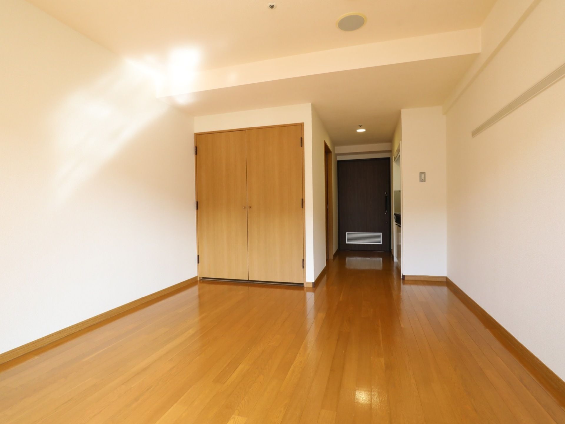 白と木目を基調とした、ゆったりとした空間の居室である。ミニキッチンや広々とした両開きの収納棚を備えている。