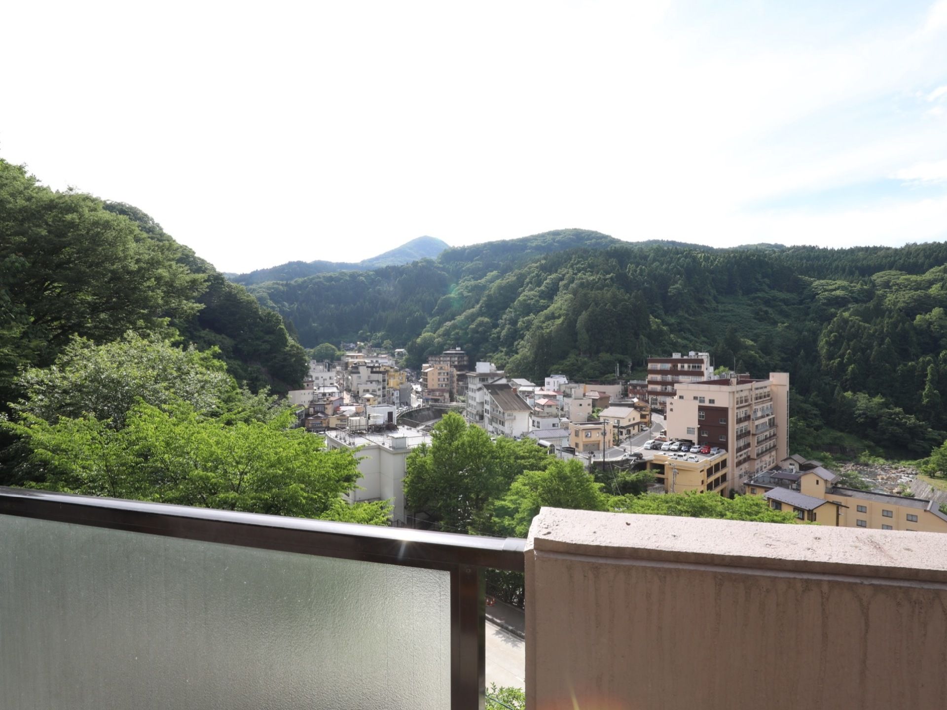 施設の上階から眺めた周辺風景である。山々が連なり、高い建物や一軒家などが建ち並んでいる。緑豊かな環境である。