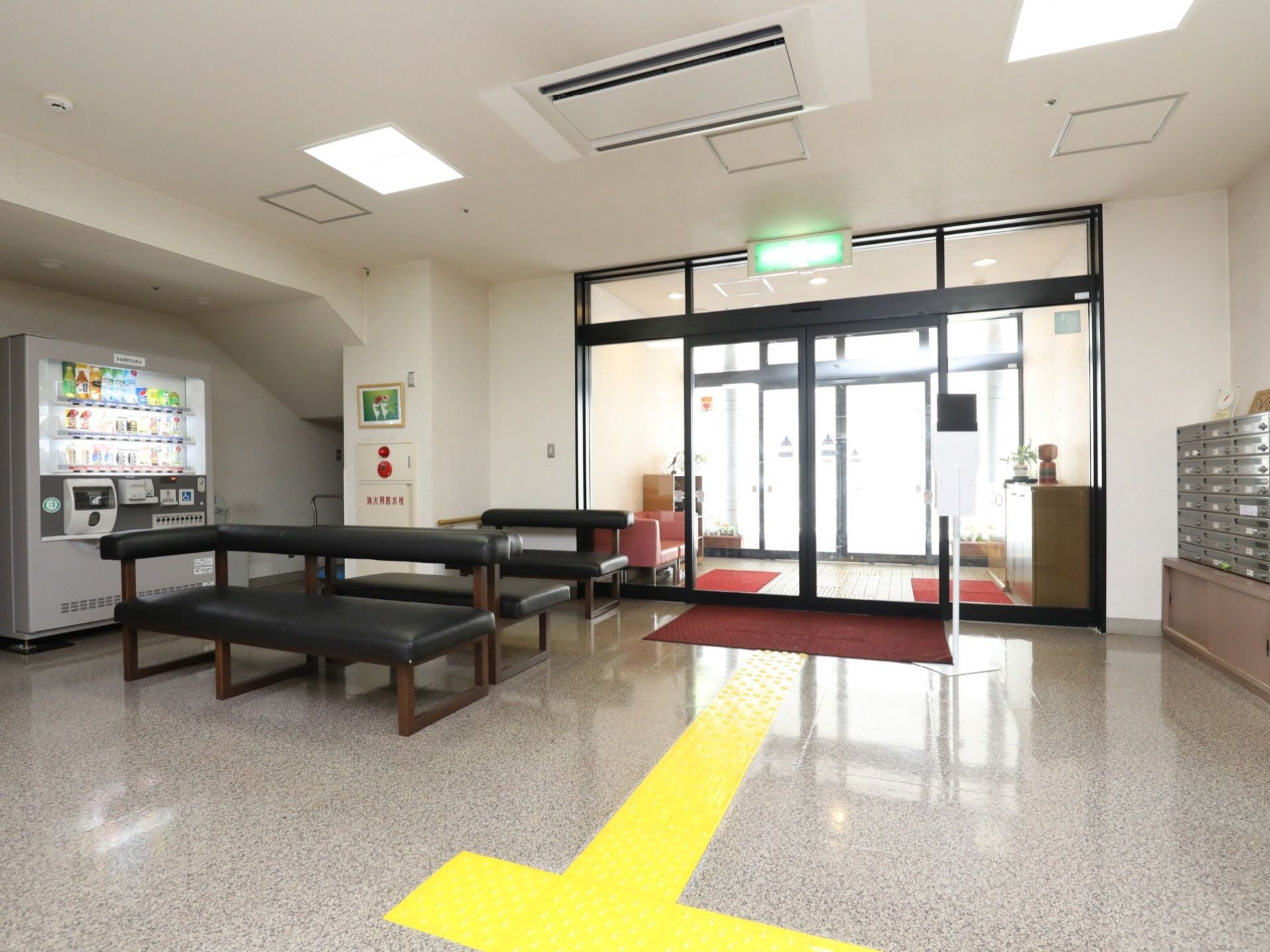 玄関には、黒枠のガラス張りの二重ドアを採用している。入ってすぐの所に黒の長い椅子を備え、壁に自動販売機を設置している。