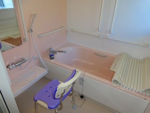個浴室には、大きめの浴槽に蓋が用意されている。洗い場スペースには壁面に鏡とシャワー、洗髪用テーブルがあり、前に入浴用の椅子が１脚置いてある。