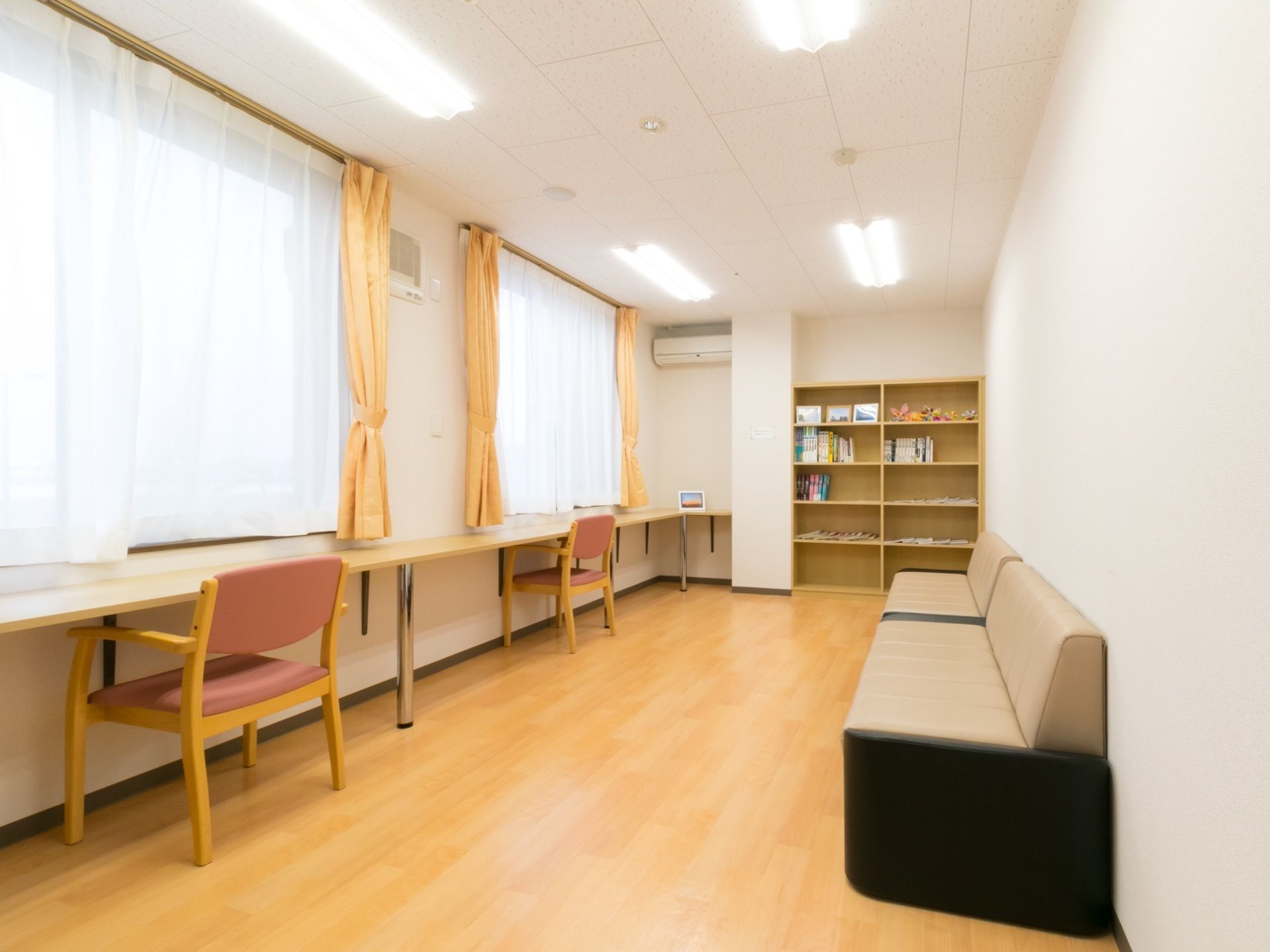 窓際には長い机があり、椅子が２脚とソファが設置されている。棚には本が数冊置いてある。エアコンが取り付けられている。