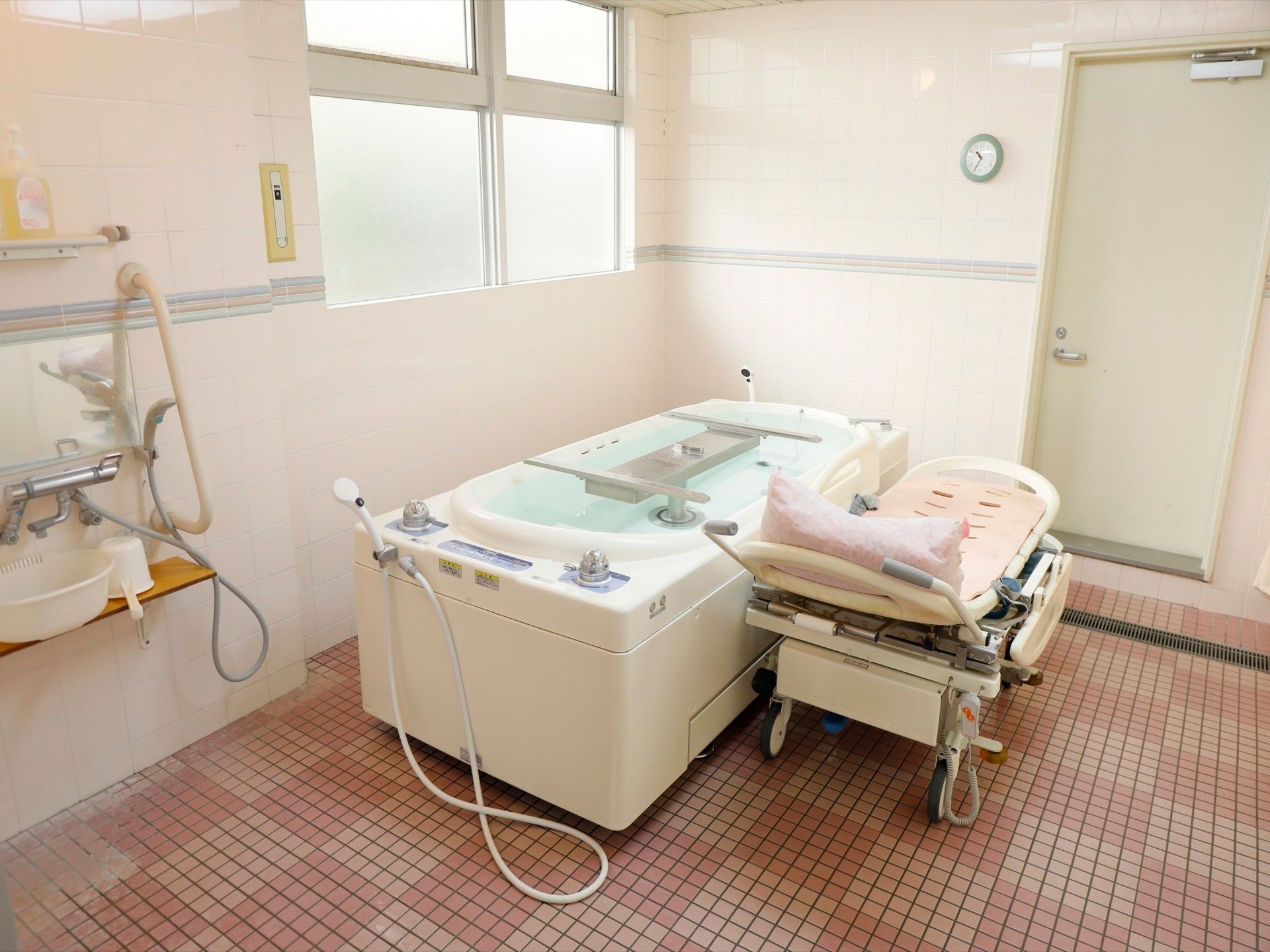 ピンク色のタイルが明るい雰囲気の機械浴室である。浴槽は仰向けで入浴するタイプで、負担なく体を温めることができる。
