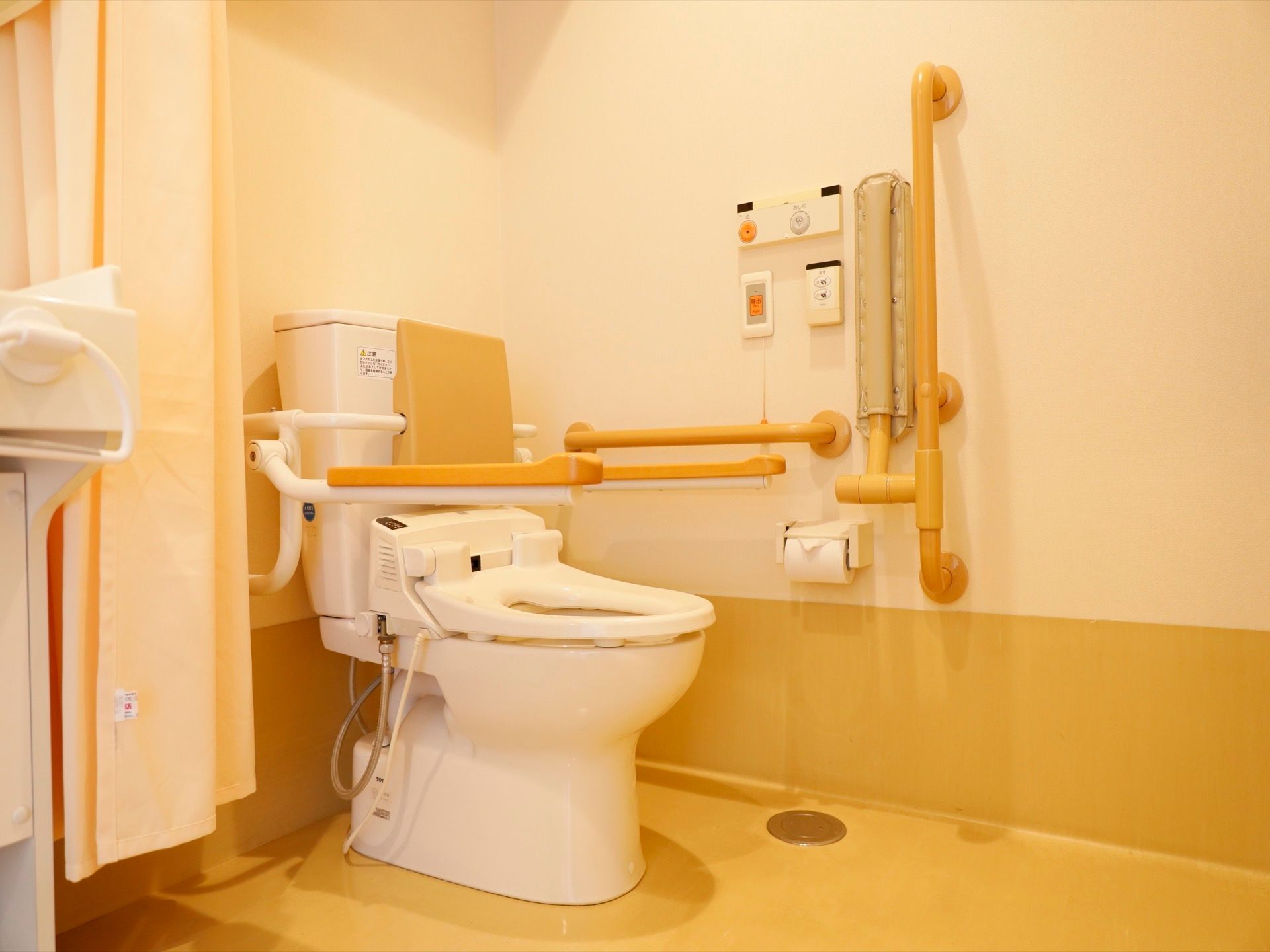 トイレの壁面には手すり、緊急ボタンが設置されている。便座には肘掛け、背もたれがあり、体に負担なくゆっくり掛けていられる。