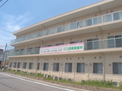 道路沿いの２階のバルコニーに、入居者募集の垂れ幕が出ている施設外観