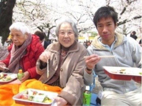 満開の花の下でお弁当を食べている女性入居者様と男性スタッフ