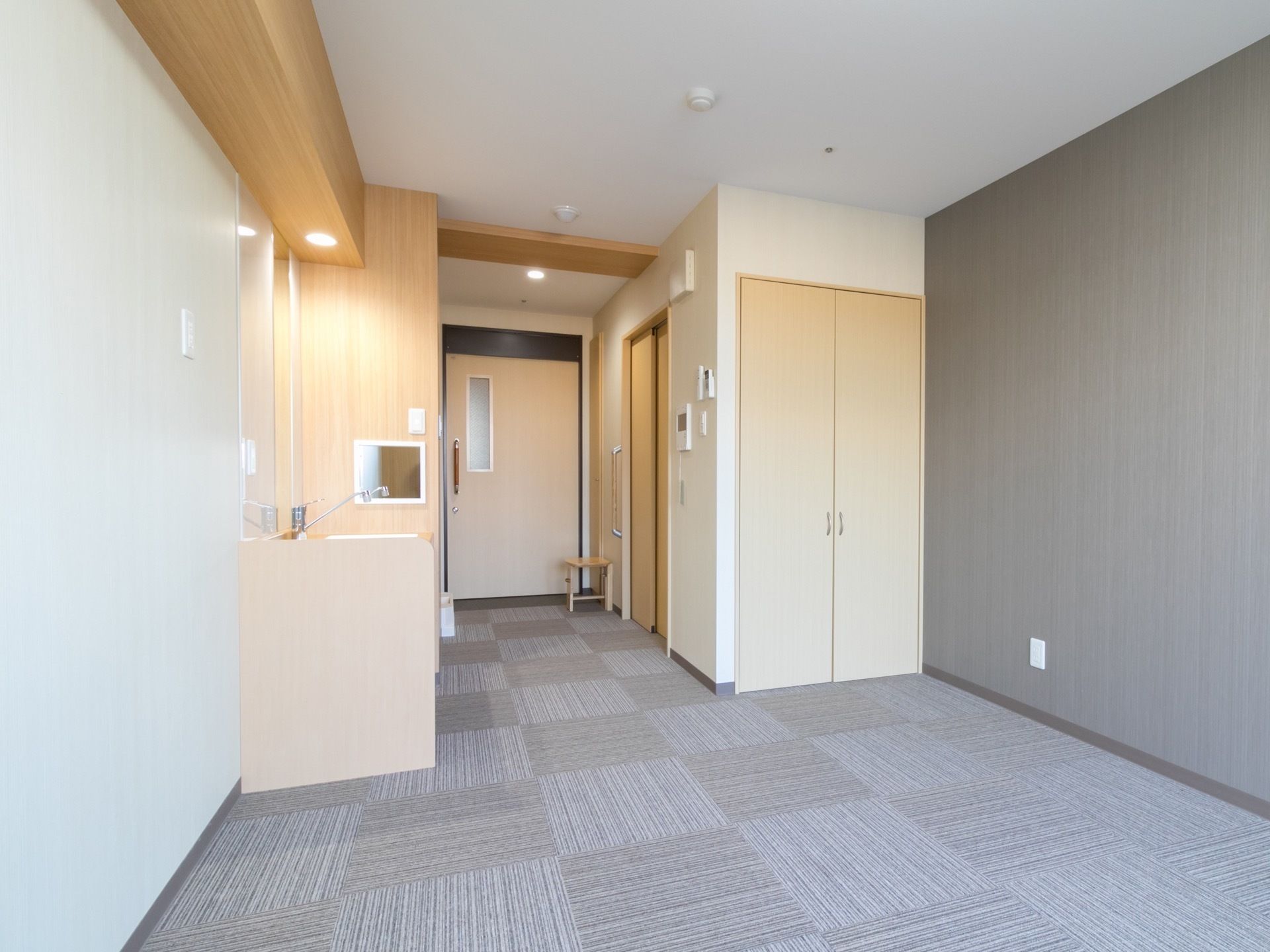 居室の壁はグレーと白色の2色に買われている。床にはグレーのタイルカーペットが敷かれている。洗面台もある。