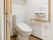 トイレには洋式便器が設置されている。タンクの上側には収納棚がある。壁側には手すり、呼び出しボタンが取り付けられている。