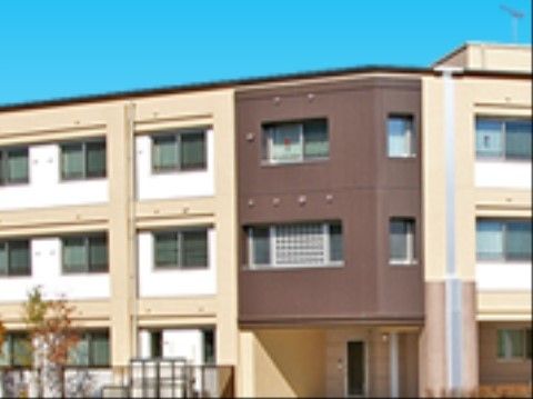 玄関上部が茶色の外壁になっている３階建ての施設外観