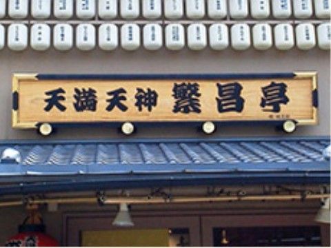 木材を使用した看板に太文字で施設名が書かれおり、上部には複数の提灯が飾られている。ブルーの屋根が印象的な建物。