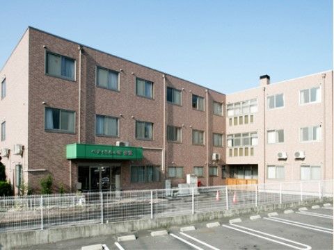 日当たりの良いグループホームである。玄関には緑色の屋根が付いており、施設名が書かれている。入口はガラス張りの自動ドアとなっている。