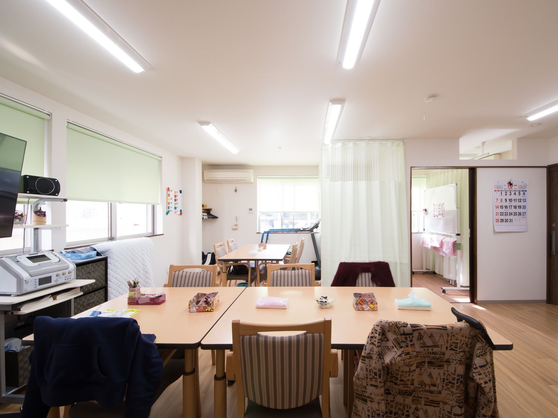 二つの部屋がつながった共有スペースにテーブルセットが3脚ある。窓にはウグイス色の遮光スクリーンがかかり、エアコンもついている。