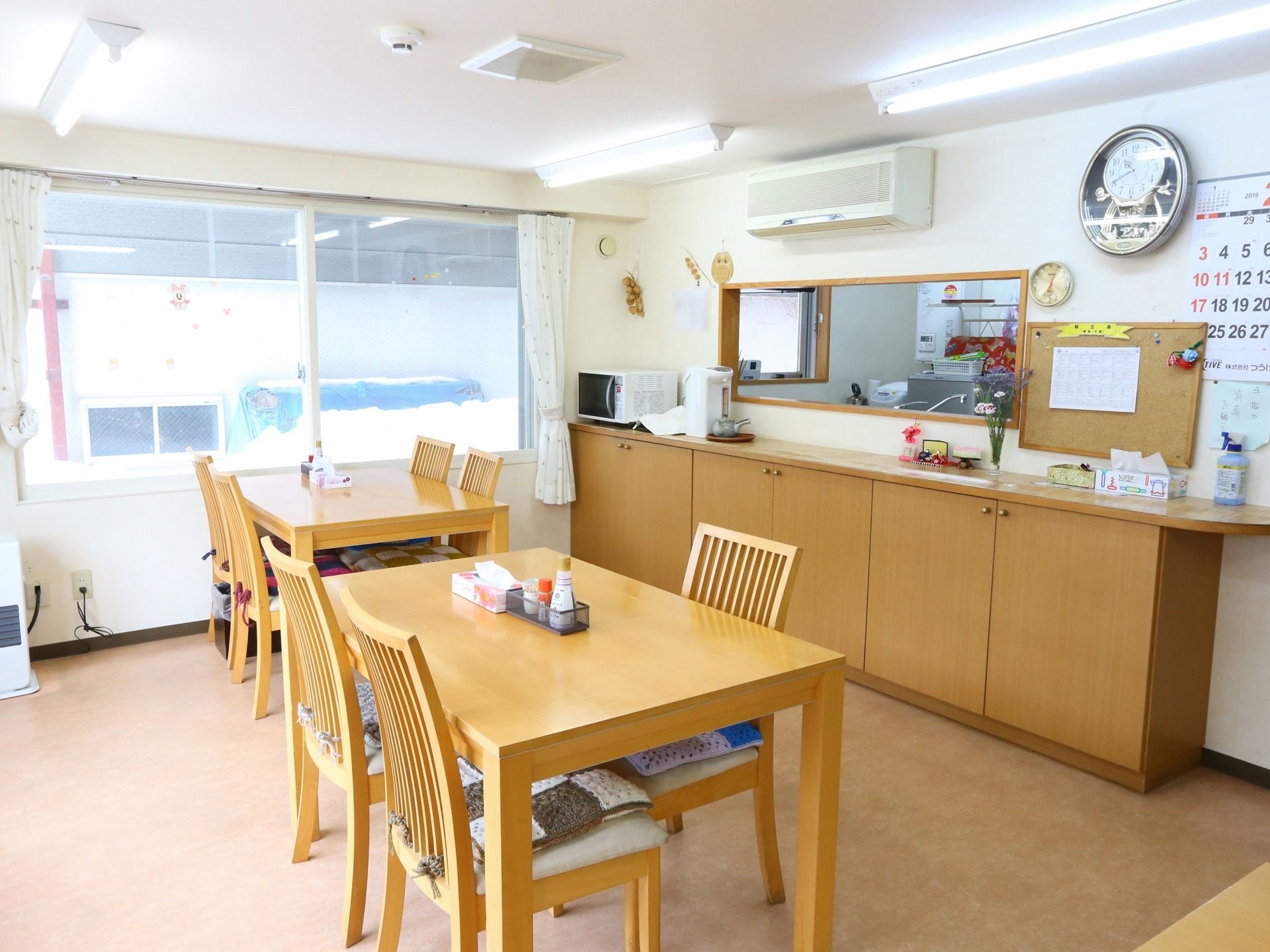 ４人掛けのテーブルと椅子が置かれている食堂。厨房へと続くカウンターがあり、手前には棚が設置され、電子レンジやポットが置かれている。