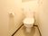 白い壁に囲まれた居室のトイレがある。床はベージュの市松模様になっている。便座には蓋があり、温水洗浄機が付いている。