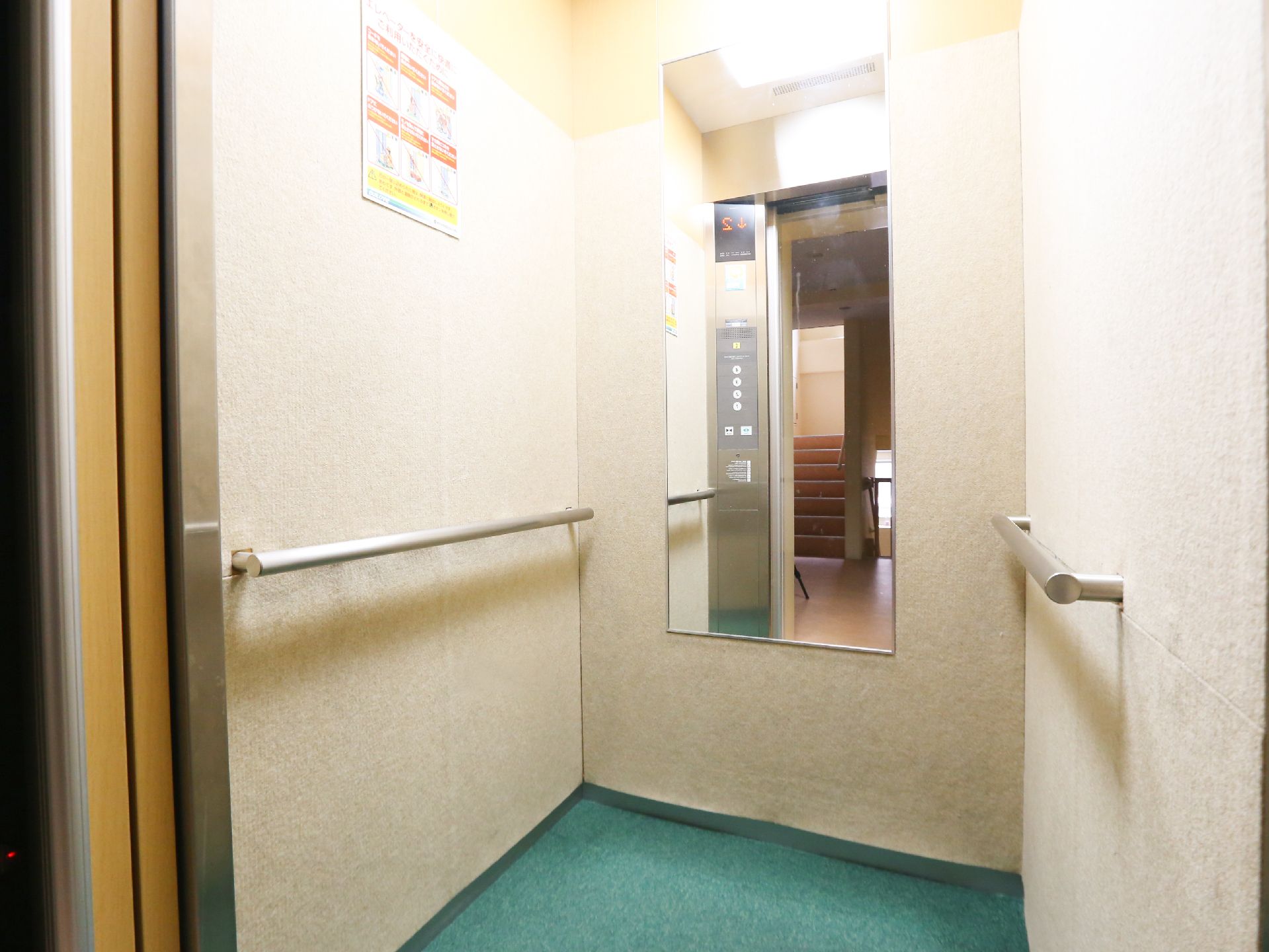 正面に大きな鏡、両側の壁に手すりが設置されているエレベーター内部