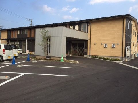 ベージュの壁に所々墨色を使った真新しい和風の建物で、２階には面格子も見える。玄関までは緩やかなスロープになっている。