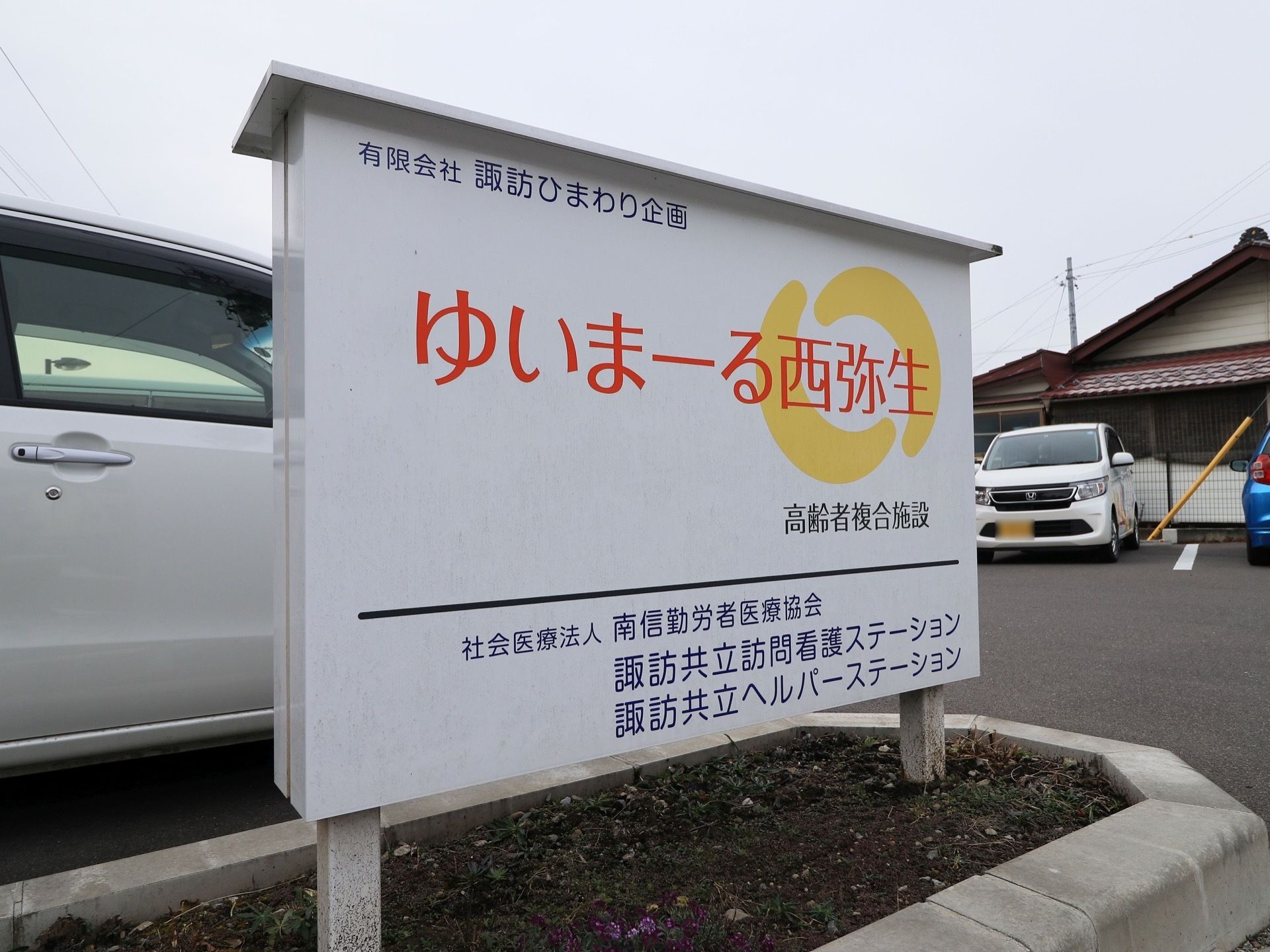 白い看板に施設名称と施設種別がロゴマークとともに記載され、敷地内に立てかけられている。白地のため見やすい。