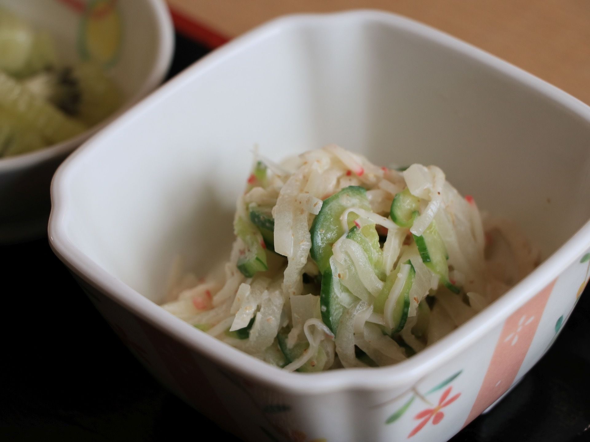 ある日の食事メニューの一品である。練り物と野菜の酢の物が、花柄の四角い小鉢に盛りつけられ置かれている。