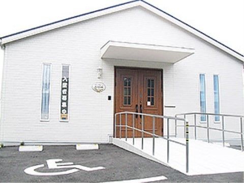 真っ白な外観が印象的な建物で、木材を使用したアンティークな扉がアクセントになっている。スロープも完備。