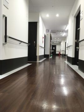 廊下の両側に居室の扉が並んでいる。壁に手すりが取り付けられ、各部屋の扉の横にネームプレートが貼られている。