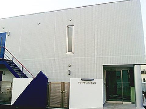 白色の外壁に長方形型の施設が建っている。左側には外階段を設置しており、玄関を介さずに出入りすることができる。