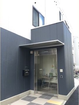 ガラス製自動ドアの扉の前は、グレーと白のタイルが格子状に張られている。壁も2階部分は白、1階部分はグレーで統一感がある。