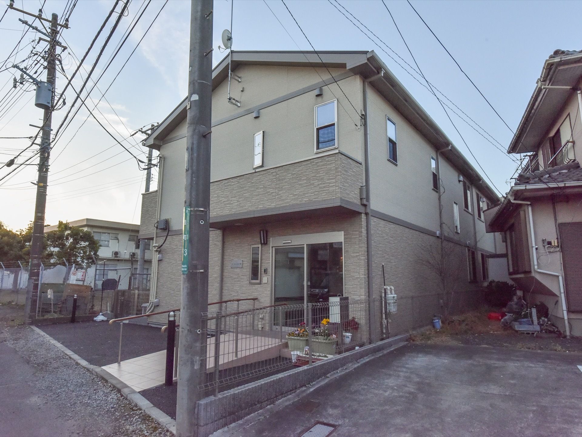 施設は住宅地の一角にある。２階建ての建物で、外壁はベージュ色をしている。敷地の入口両側に、電信柱が立っている。