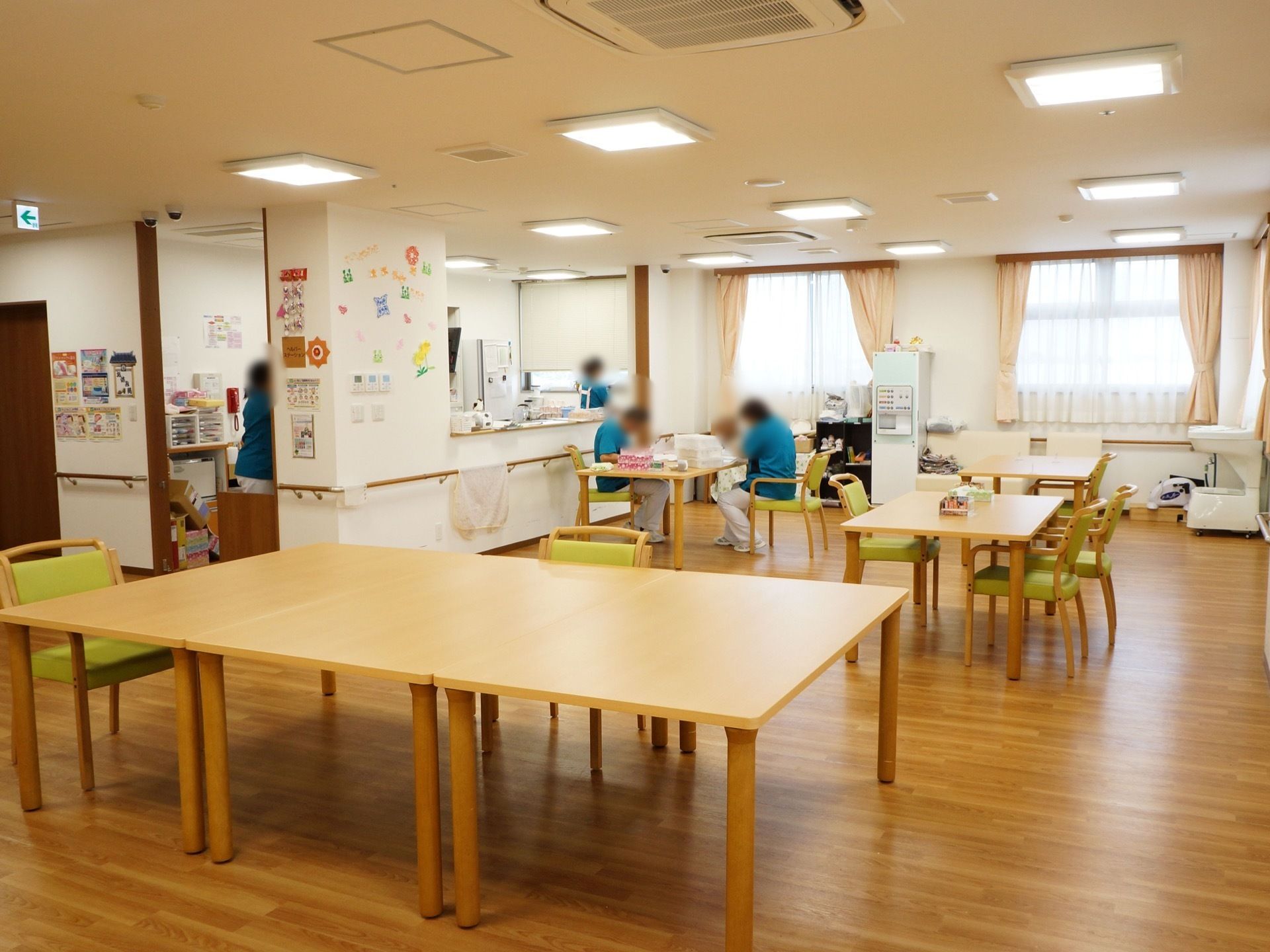 木目調デザインのテーブルの周りに、黄緑色の椅子がセットされている。青いポロシャツを着たスタッフが、奥のほうに数名いる。