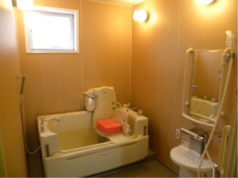 個室タイプの明るい機械浴室である。洗い場には鏡が取り付けられており、周りに白い手すりが設置されている。