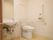 洋式の便器と洗面台が設けられたトイレの個室である。壁にはL字型の手すりや緊急時呼び出しブザーが取り付けられている。