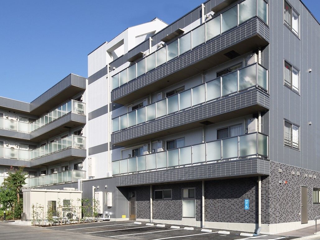 グレーの建物で居室の部分が白くデザインされている。建物に隣接して駐車場が設置されているため、車に訪れやすい。