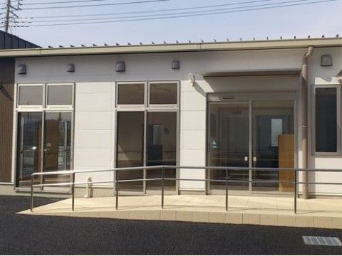 平屋建てのグループホームである。ガラス張りの自動ドアの前には、手すりが取り付けられたスロープが設置されている。