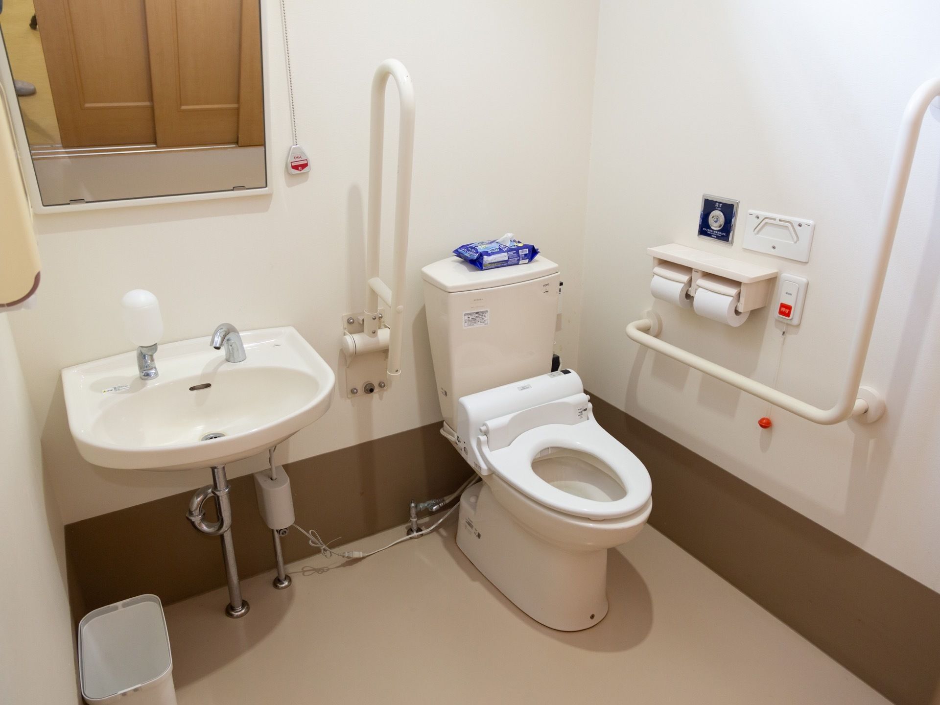 白色の洗面台が備えつけられた、広々としたトイレである。可動式の手すりを完備。ナースコールも設置されている。