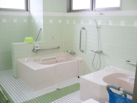 手すり付きでピンク色の浴槽が２つ並んで設置されている共同浴室
