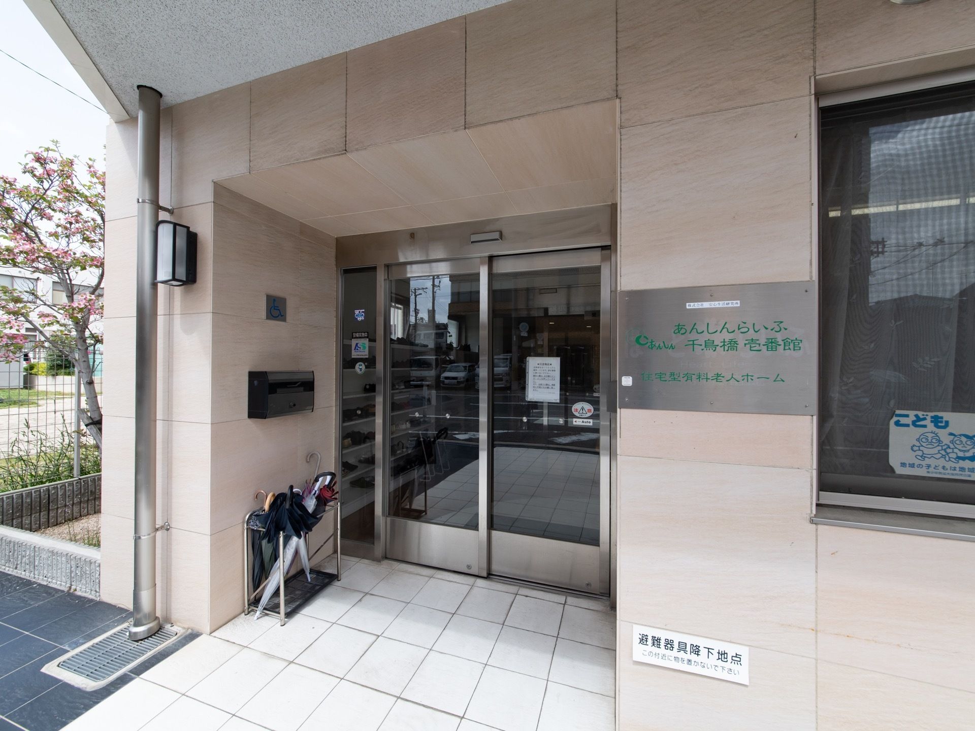 外から見た玄関口の様子。メタルプレートが看板として壁に取り付けられており、緑色の文字でロゴが書かれている。