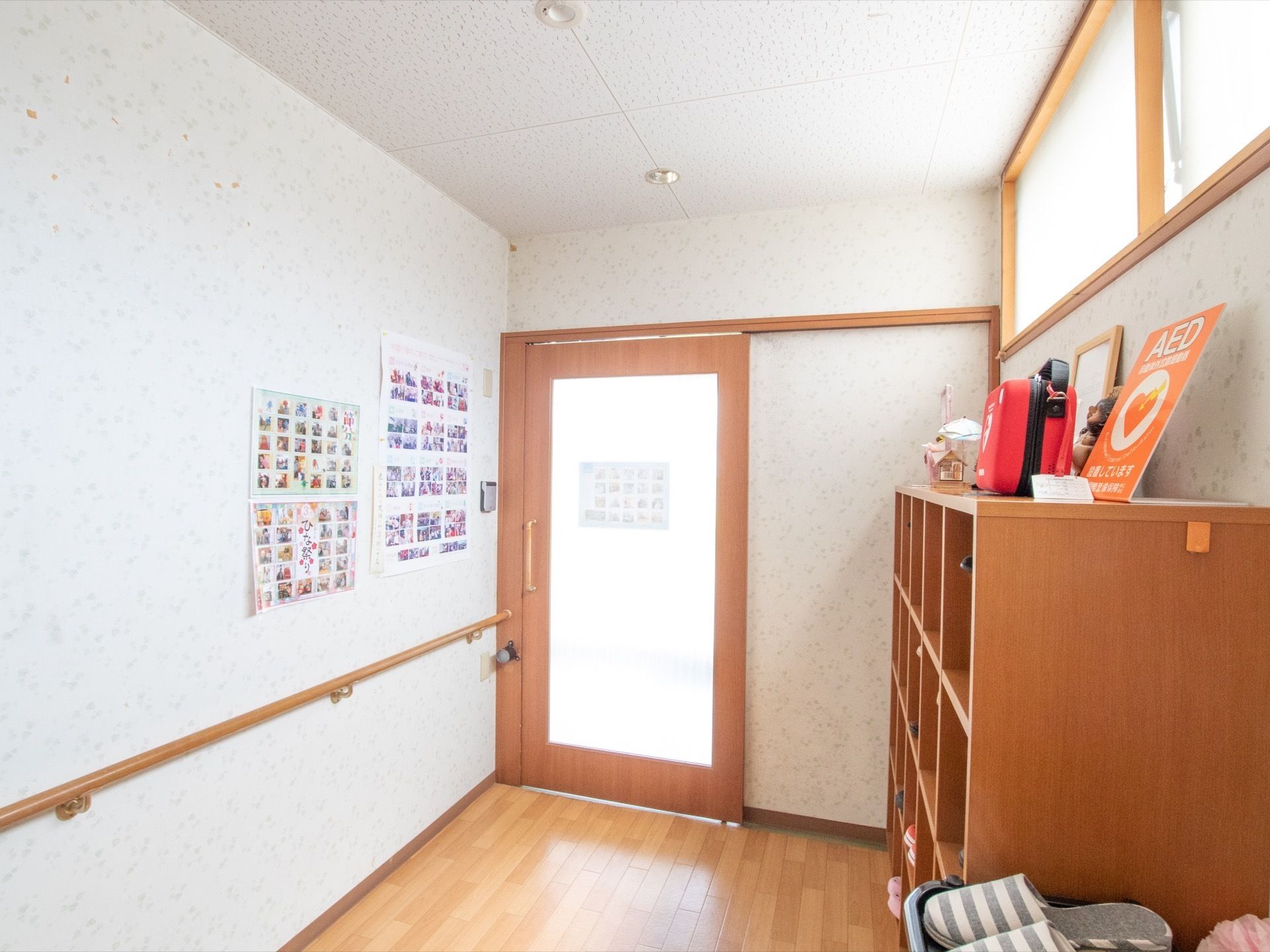床はフローリング敷きで、天井と壁は白で統一されている。壁には手すりが付けられ、靴箱の上に赤いバッグに入ったAEDが置いてある。