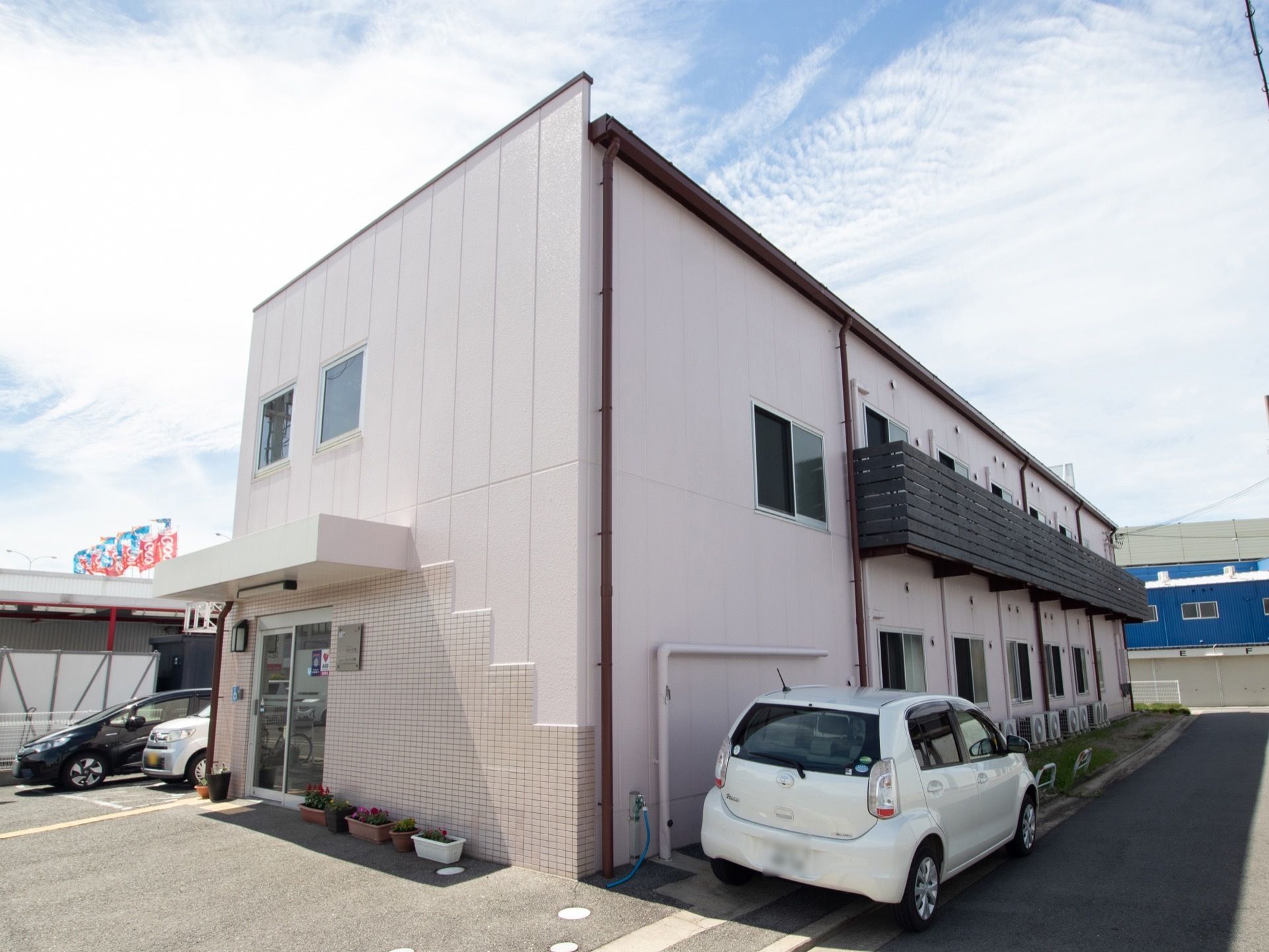 建物は総2階建てで、裏側に駐車場が備わっている。玄関ドアの上にはひさしがあり、足元にプランターが並べて置かれている。